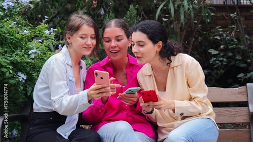 A group of three happy young females enjoying playful conversation as they interact with their smartphones, sharing moments of joy and connection through their mobile devices and applications.
