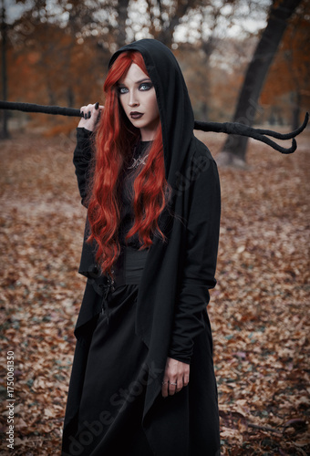 Halloween (Samhain) theme: a ginger (red-haired) witch with horned staff in forest. Portrait of attractive redhead mage in autumnal woods