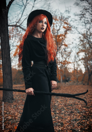 Halloween (Samhain) theme: a ginger (red-haired) witch with horned staff in forest. Portrait of beautiful redhead enchantress in autumnal woods