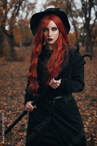 Halloween (Samhain) theme: a ginger (red-haired) witch with horned staff in forest. Portrait of beautiful redhead hex in autumnal woods