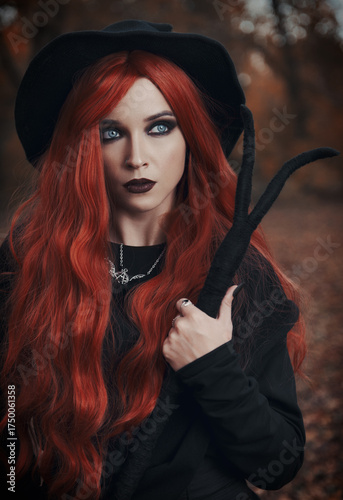 Halloween (Samhain) theme: a ginger (red-haired) witch with horned staff in forest. Portrait of beautiful redhead sorceress in autumnal woods
