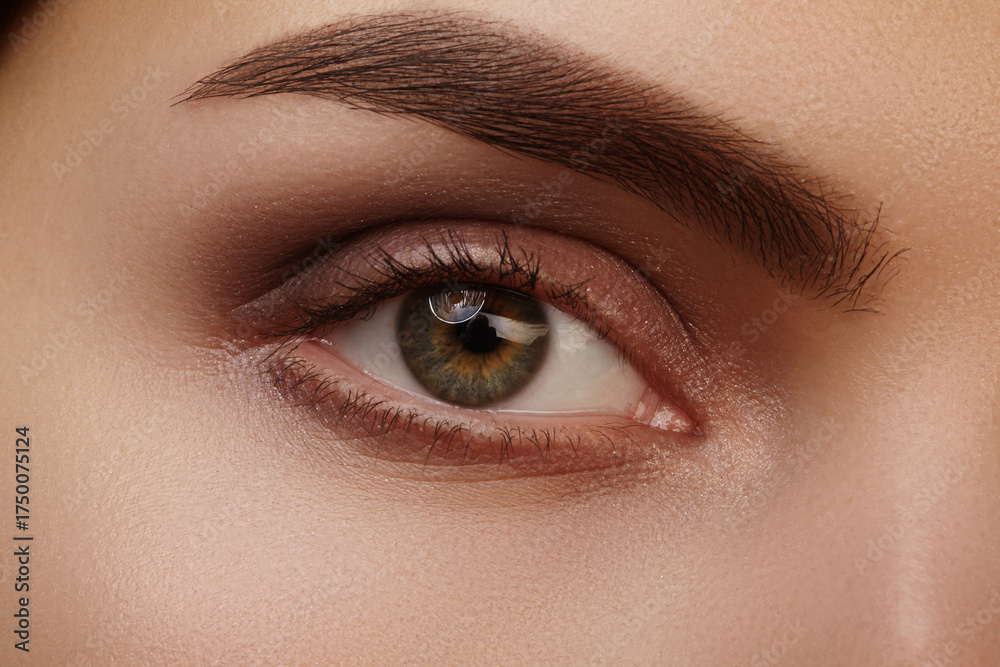 Fototapeta premium Macro close-up of a green eye with defined eyebrow and long lashes. Hazel iris detail, fashion makeup and gaze for beauty and health imagery. Concept for vision clinic, beauty salon, permanent make-up