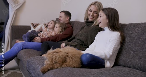 Happy family at home sitting on the sofa with the dog and watching tv