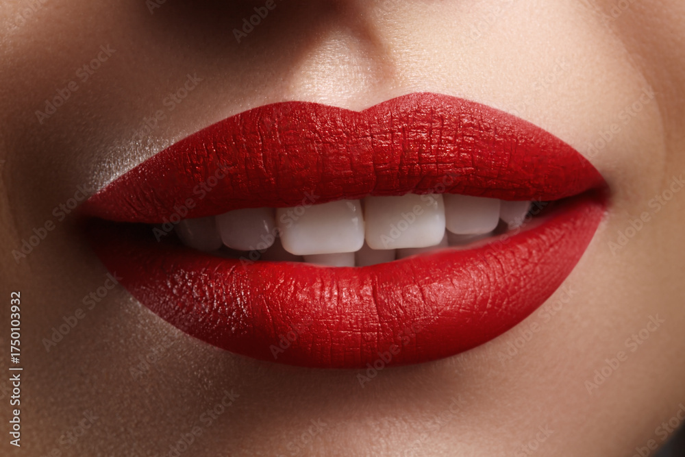 Obraz premium Macro shot of glossy matte red lips parted to show white teeth. Studio-lit close-up emphasizing lip stick texture, shine and color contrast. Ideal for beauty, cosmetology and fashion campaigns