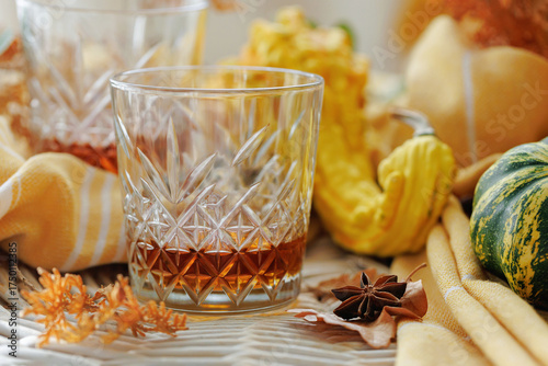 Vintage whiskey glass with amber drink on rustic autumn-themed table with gourds and spices