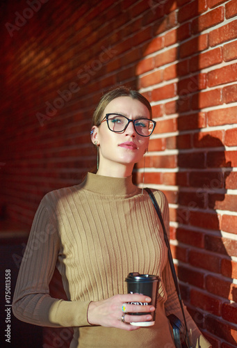 Young businesswoman wearing glasses looks confidently against brick wall in a building