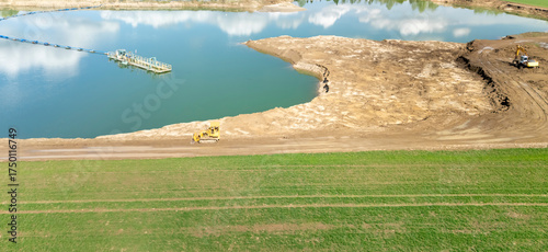 Aerial view of a construction site by a lake, showing heavy machinery working on the shoreline. This scene captures the industrial activity and environmental interaction.
