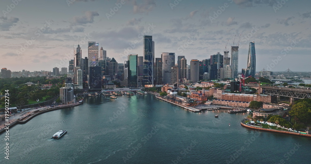 Obraz premium Australia, Sydney: Breathtaking aerial view of Sydney modern skyline city center reflecting in calm harbor waters. Iconic skyscrapers cityscape illuminated by soft sunset light. Drone panorama