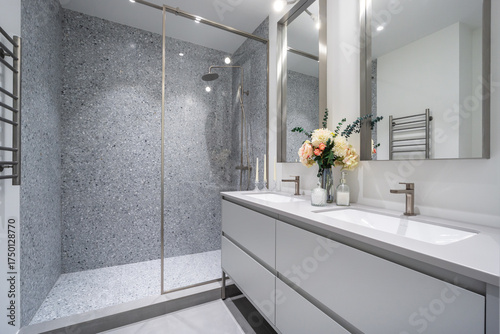A modern bathroom showcases a sleek design with a spacious glass shower, double sinks, and fresh flowers on the countertop, creating a calm and inviting atmosphere