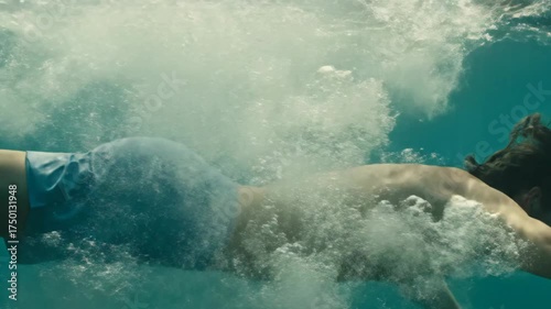 A man dives headfirst into clear blue water, swimming gracefully below.