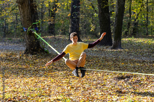 man in yellow t-shirt sitting on slackline in autumn park
