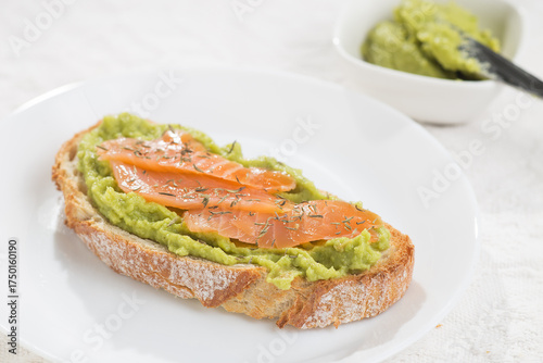 A slice of bread with avocado and salmon decorated with thyme