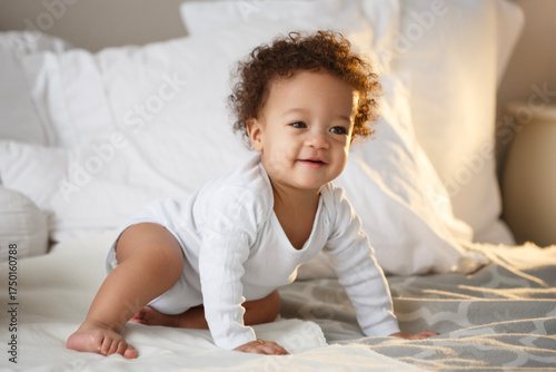 Adorable baby crawling on a cozy bed in morning light, wearing a white bodysuit. Warm natural atmosphere symbolizing family love, childhood joy, and home comfort.