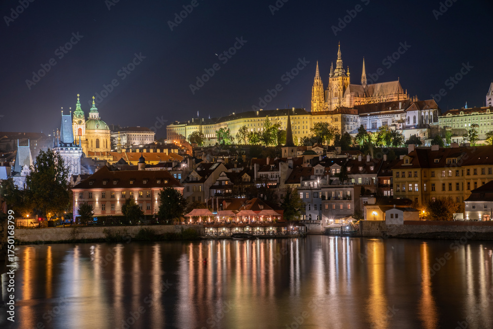 Obraz premium Night view of Prague with illuminated Charles Bridge, Prague Castle, and reflections on the Vltava River. Magical and historic European city after dark.