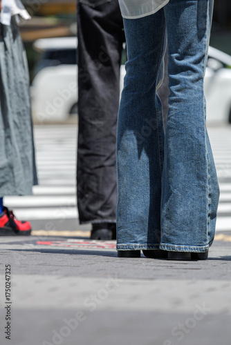 Bell bottom jeans and platform shoes reminiscent of 1970s fashion adorn a young Japanese woman waiting at a crosswalk in a busy urban setting.
