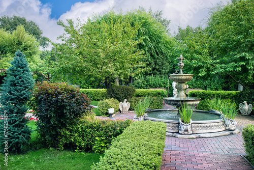 A beautiful garden landscape with a green lawn, hedge, bushes and trees.