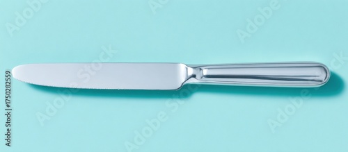 A single silver butter knife on a turquoise background.