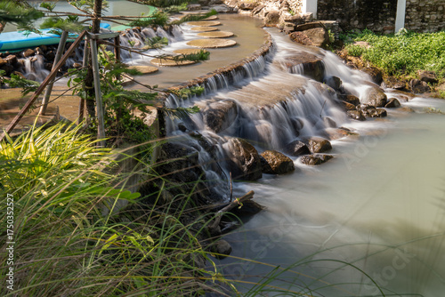 Scenic shot of a slow-shutter waterfall framed by soft-focus plants in the foreground. Taken at a serene resort in Nakhon Nayok, Thailand.