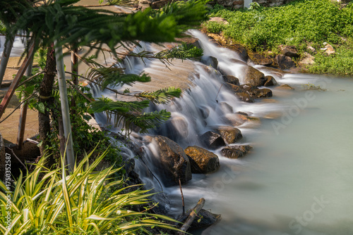 Scenic shot of a slow-shutter waterfall framed by soft-focus plants in the foreground. Taken at a serene resort in Nakhon Nayok, Thailand.