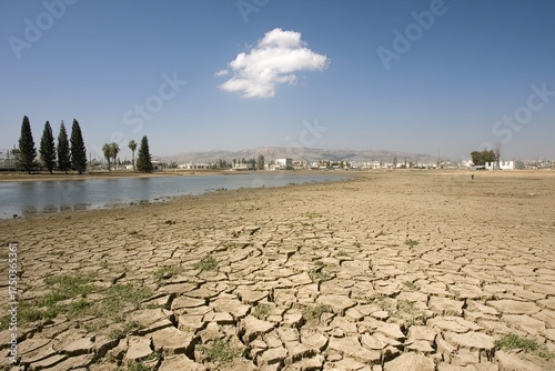Cracked dry earth by lake with building silhouettes under blue sky