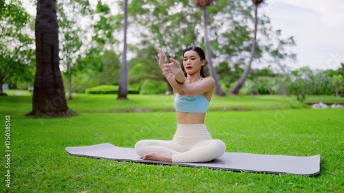 Beautiful young Asian woman practicing yoga outdoors on sunny day at public park.Serene female peaceful and mindfulness sit on exercise mat make lotus pose