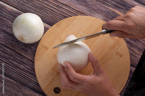 Manipulacion de alimentos, manejo de comida en la cocina, manos cortando cebolla blanca sobre una tabla de cortar en una mesa rustica de madera, vista aerea, o top view flat lay
