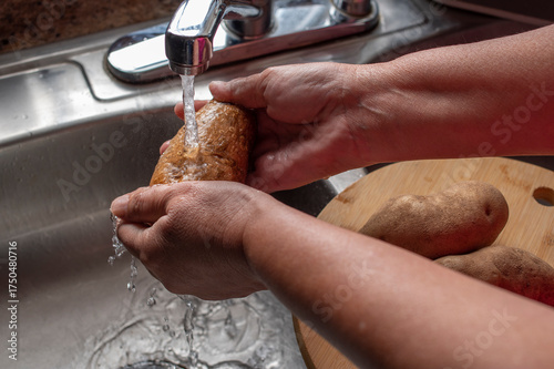 Manipulacion de alimentos, manejo de comida en la cocina, manos lavando una papa con agua de la llave 
