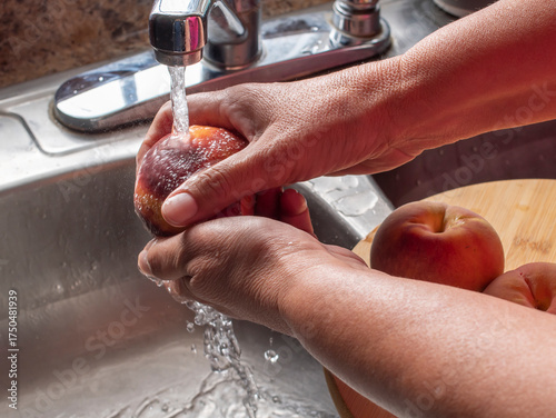 Manipulacion de alimentos, manejo de comida en la cocina, manos lavando un durazno con agua de la llave