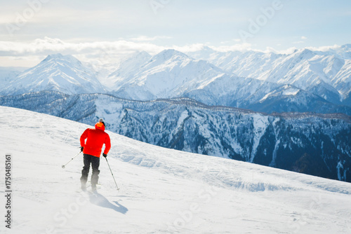 Male adult skier in red jacket go freestyle off piste carving turns to fresh powder mountainside in snowy mountain resort during sunny winter day adventure in alpine high mountains