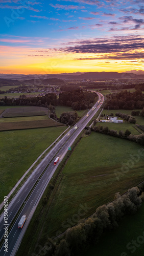 An aerial view of the highway cutting through the picturesque Slovenian countryside near Krtina village by Lukovica, bathed in the warm glow of sunset.