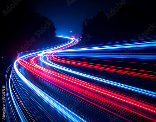 Long exposure captures red and blue light trails from vehicles moving along a winding road at night, surrounded by dark trees.