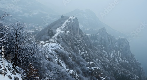 Snow-Covered Rocky Mountain Ridge with Sparse Trees in a Misty Winter Landscape