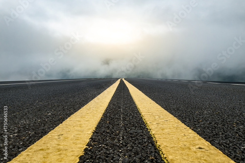 Asphalt road with yellow lines disappearing into foggy distance under bright sky