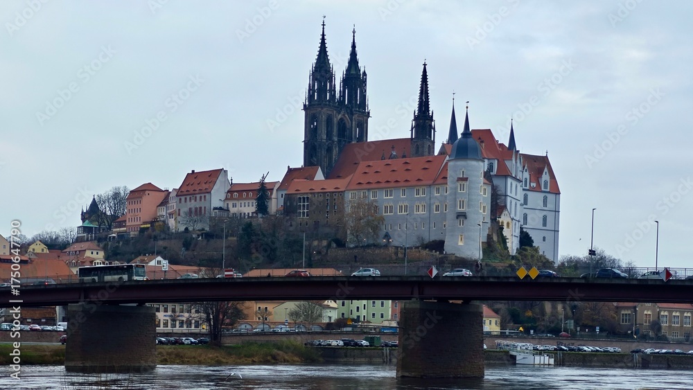 Fototapeta premium Panoramic view of Meissen, Germany features Albrechtsburg Castle and Meissen Cathedral atop a hill. The castle's Gothic architecture stands prominently with tall spires and intricate details. 