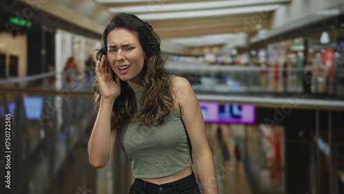 Free Download Woman cups her ear with her hand while squinting in a busy indoor shopping mall building; curiosity. - GFXLoad