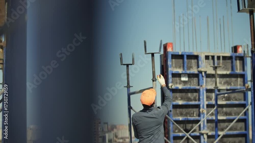 Construction worker in orange helmet installing metal support at building site