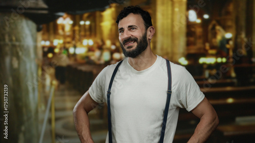 Quadro su tela Hispanic man with beard in white shirt smiling confidently inside a traditional catholic church with ornate architecture and warm lighting