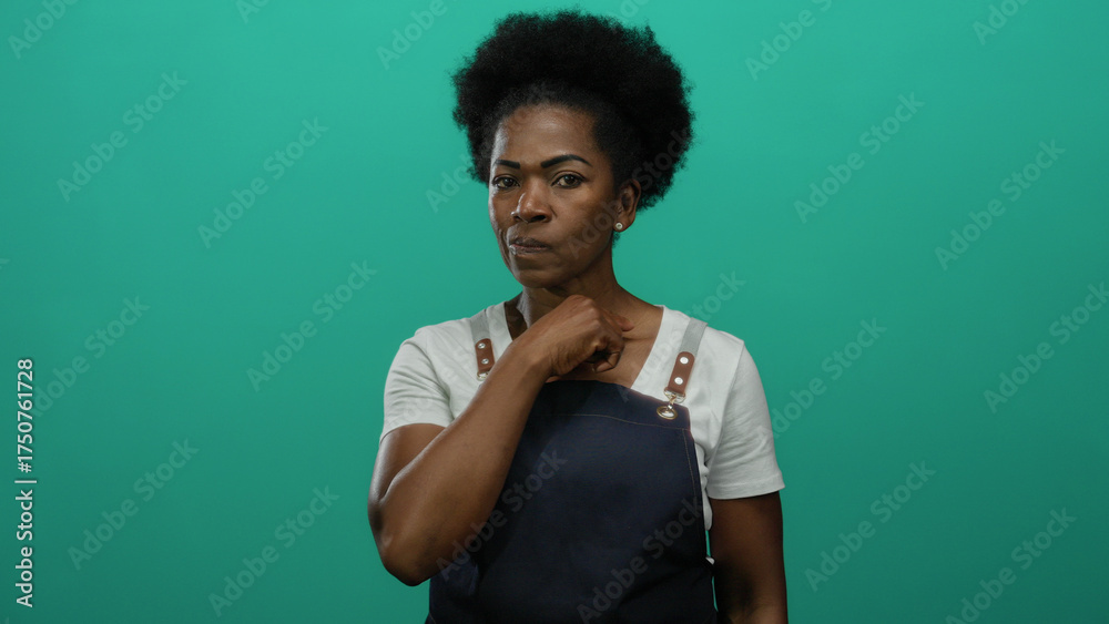 Φωτογραφία Woman in apron gestures vigilance and threat against isolated green background, expressing assertive communication through expressions and hand signs with an intense focus