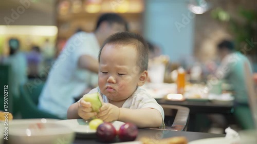 Asian baby eating cantaloupe in a restaurant, seated in a high chair, one-year-old boy