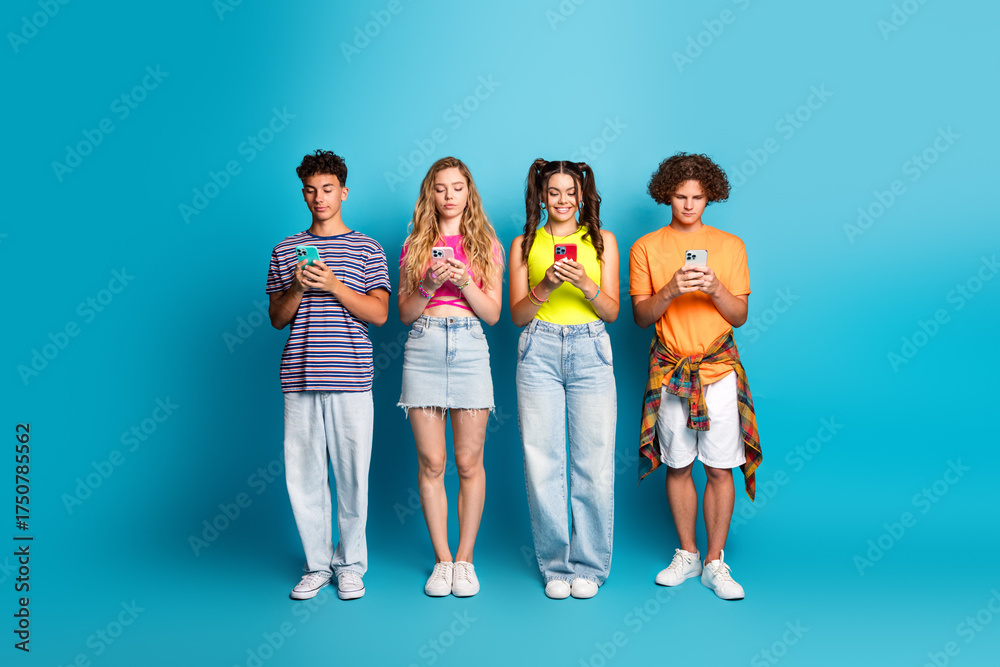 Fototapeta premium fun and friendly teens on a bright blue backdrop absorbed in their phones creating a playful modern youth moment