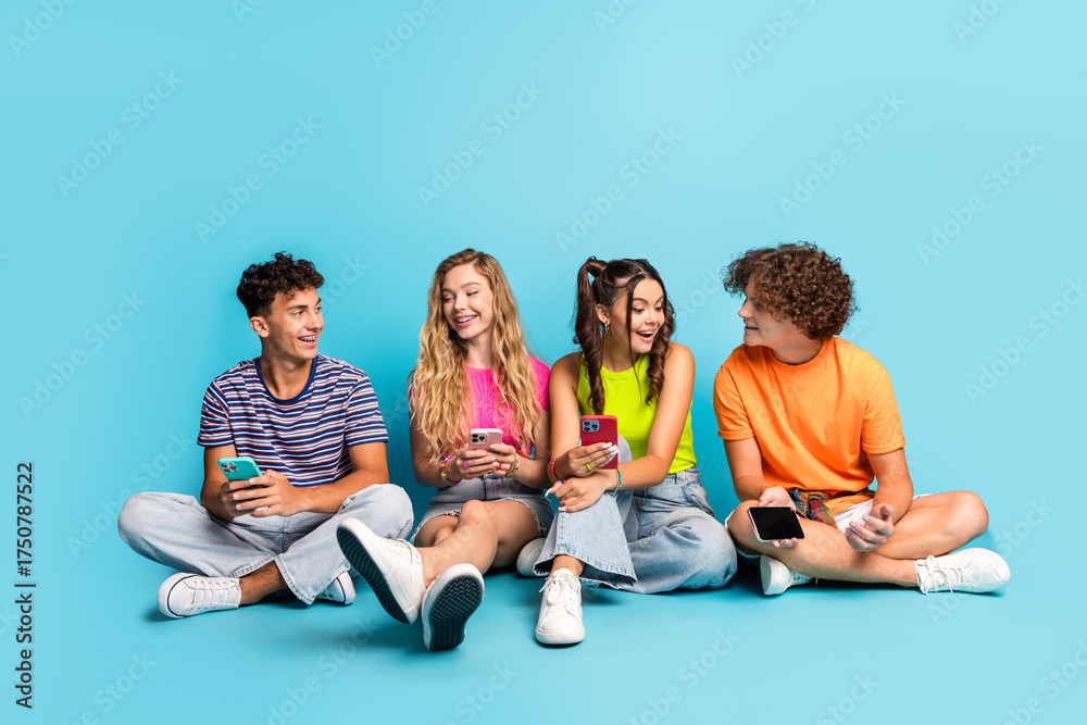Obraz premium Funny teen friends hangout on a bright blue set chatting and smiling while phones glow with colorful screens in a sunny casual vibe
