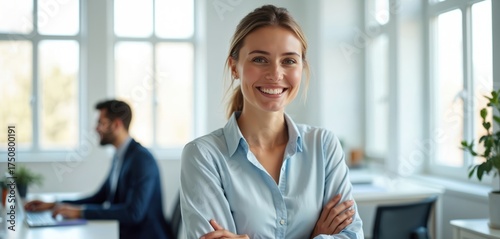 Smiling woman with crossed arms in a modern office space. Coworkers collaborate in background. Represents successful business, teamwork, and pro career growth.