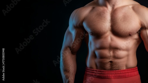 A muscular young Caucasian male with a defined physique poses against a black background