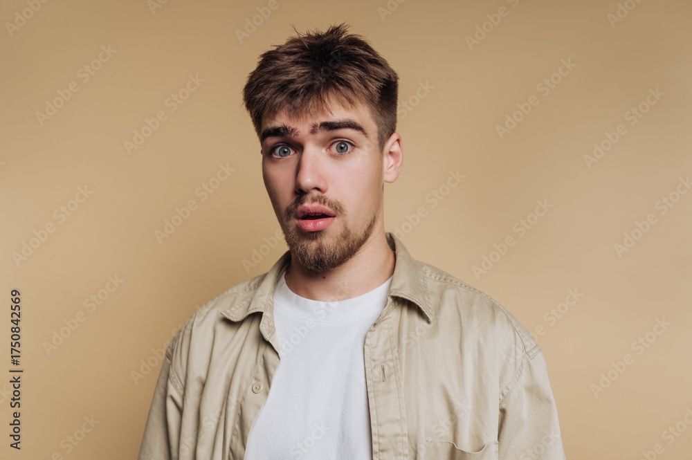 Obraz premium portrait of young man shows a surprised expression, embodying shock and curiosity on beige background