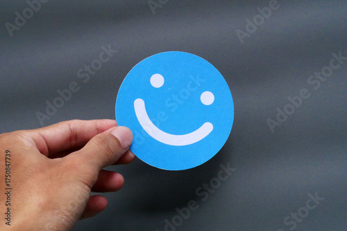 A person's hand holding a blue smiley face icon against a simple gray background