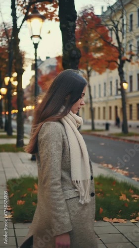 Young woman walking in autumn park with fallen leaves and lampposts  