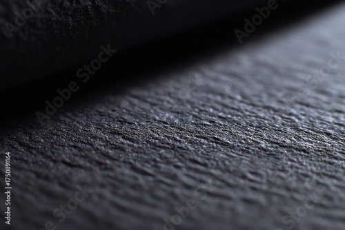 Close-up of a textured black surface with subtle lighting, highlighting roughness and fine details in a shallow depth of field