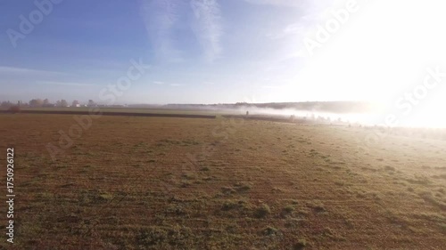 Drone flight over autumn fields. FPV drone flies at dawn in autumn. Aerial flight over a field through the morning fog toward dawn. The sun's rays illuminate the layer of fog. Autumn landscape.