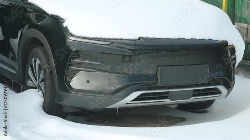 Abandoned electric car in outdoor parking lot on winter day. Covered in layer of snow, vehicle sits motionless. Electric cars often experience breakdowns, short circuits during cold, frosty season.
