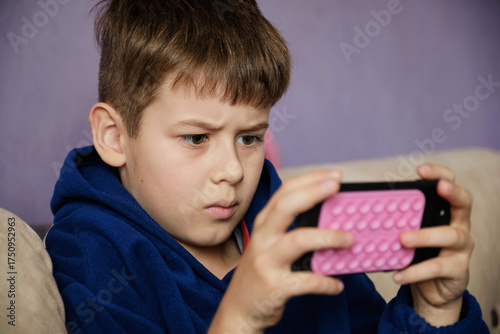 Young boy engrossed in watching a video or playing a game on a smartphone.